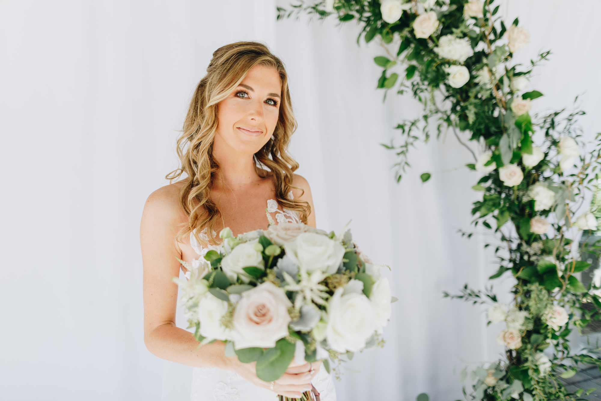 Bride with bouquet and floral arch at backyard wedding