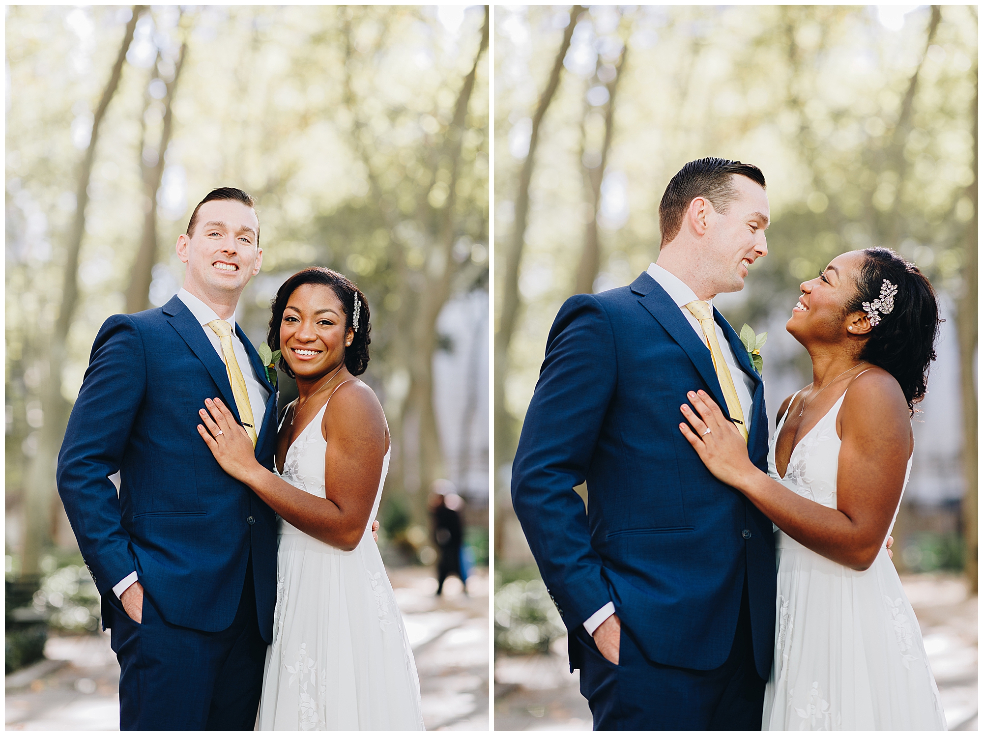 A couple in wedding attire poses outdoors during their Wagner Cove elopement. The groom wears a navy blue suit and yellow tie, and the bride's white dress features floral hair accessories as they smile lovingly at each other amid trees.