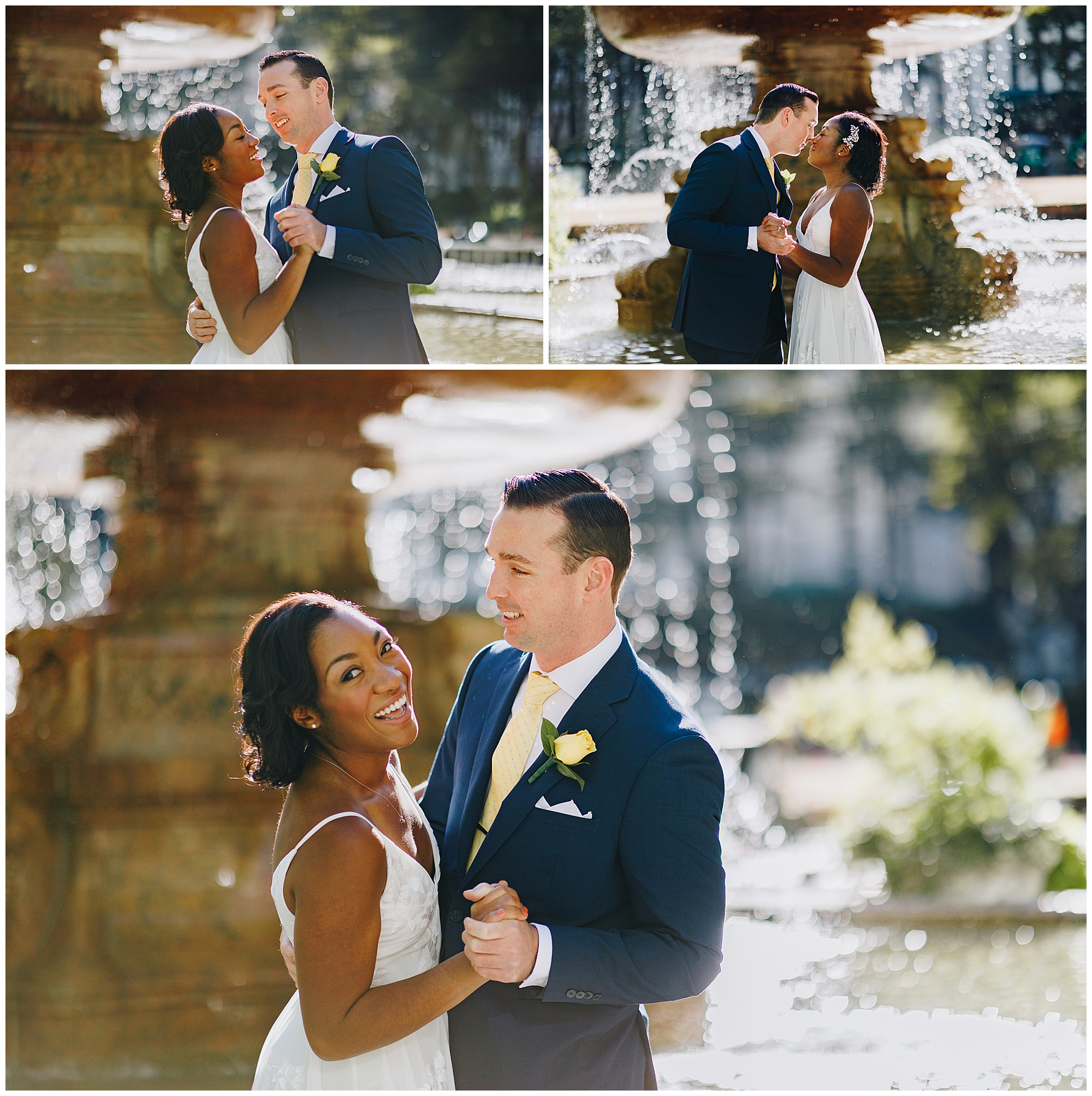 A couple dressed in wedding attire dances and smiles together in front of a sunlit fountain, capturing the romance of a Wagner Cove elopement. The woman wears a white dress, while the man sports a navy suit with a yellow tie and boutonniere.