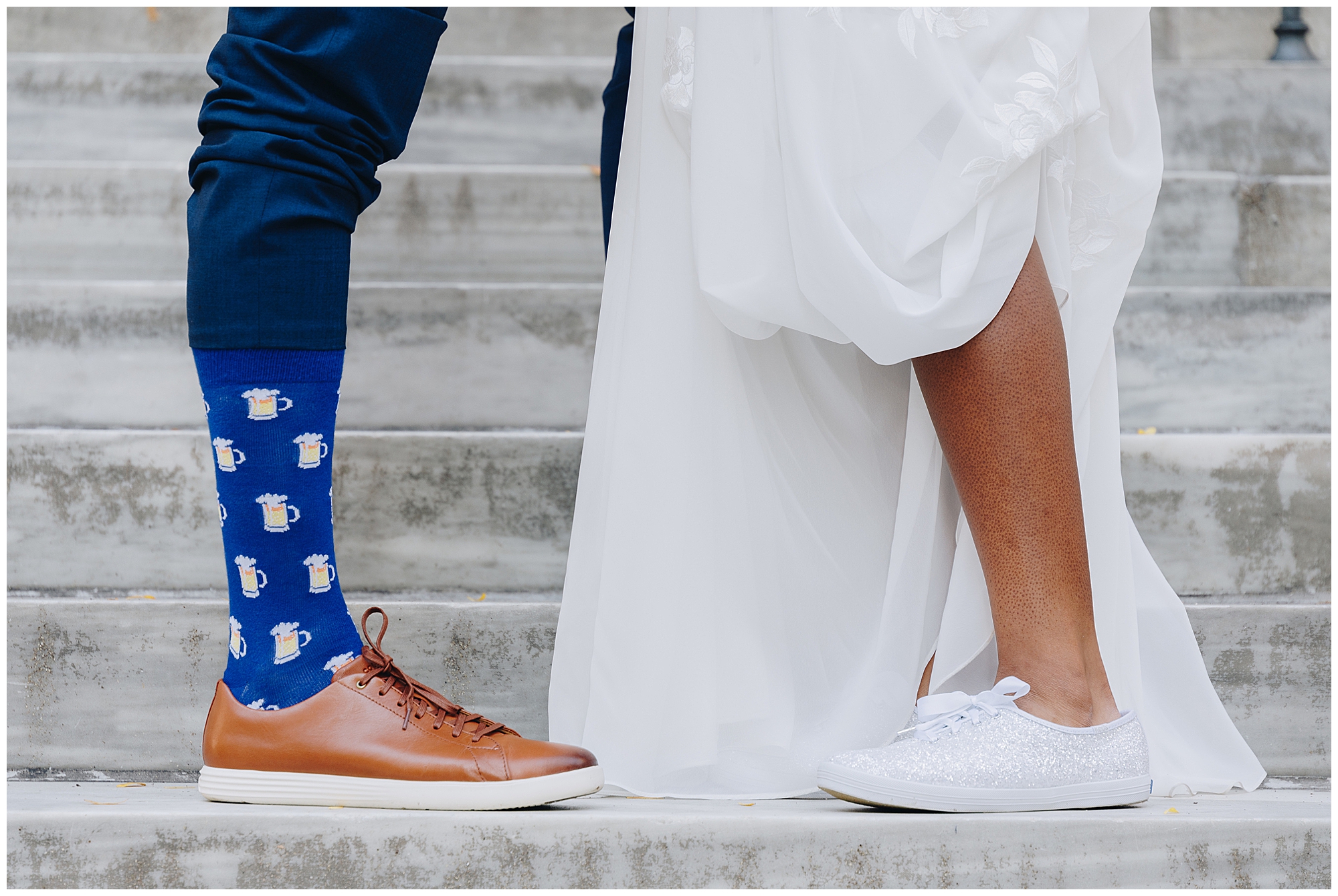 A close-up of a couple on steps: one wearing brown shoes, blue pants, and beer mug socks; the other in a white dress with sparkly sneakers. Their legs face each other at Wagner Cove elopement, suggesting a wedding or special occasion.