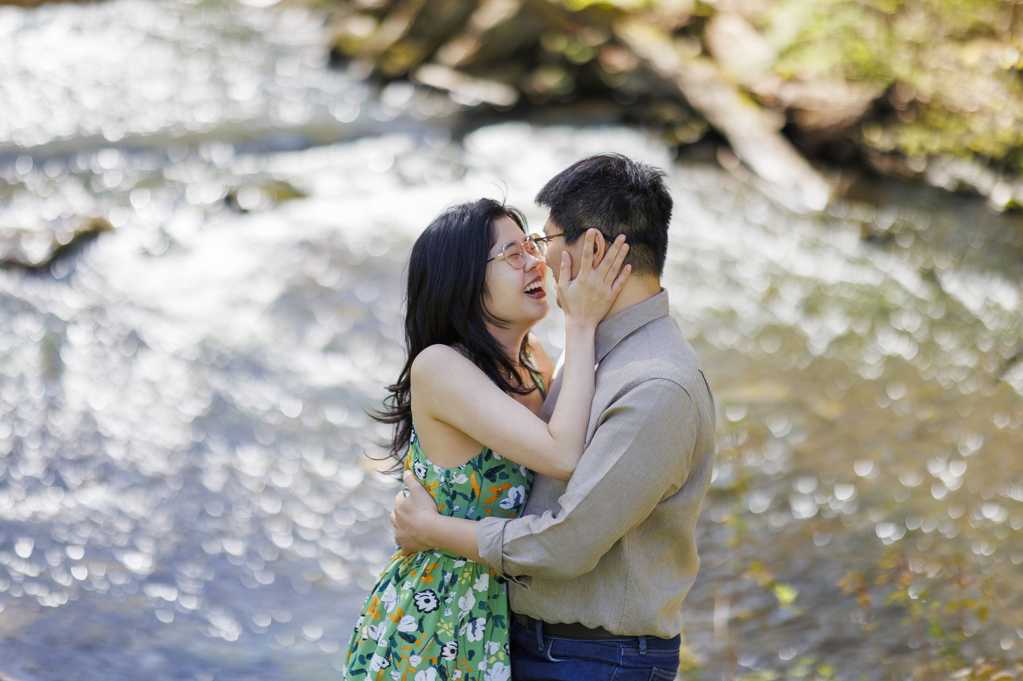 Couple laughing by river with Hudson Valley wedding photographers capturing romantic engagement moment near water and trees