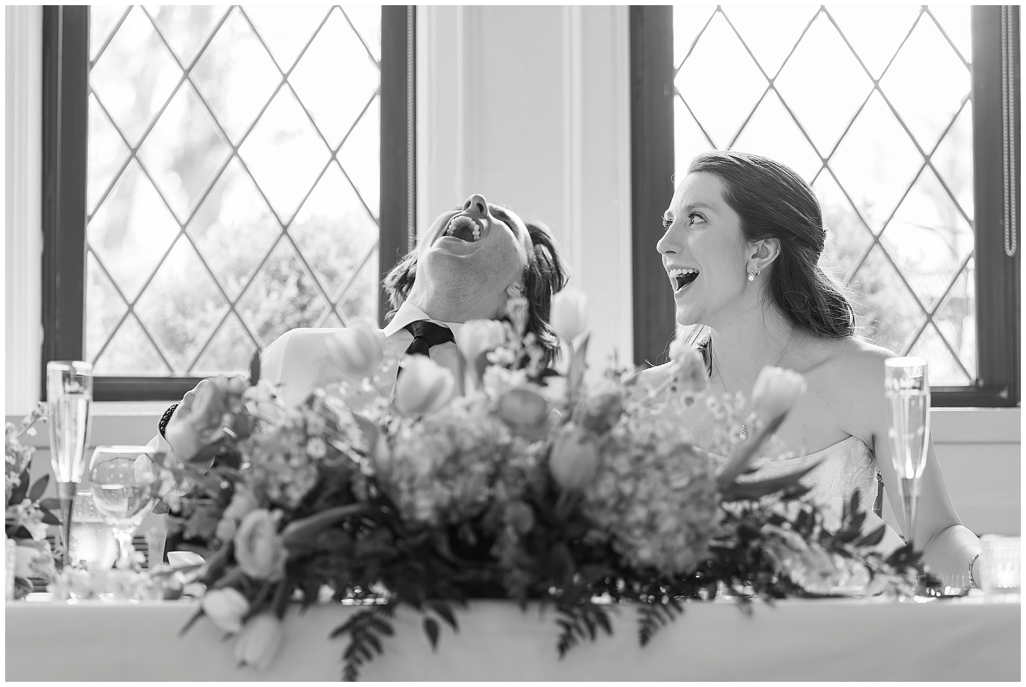 Joyful bride and groom laughing together at their wedding reception table decorated with flowers, captured by Hudson Valley wedding photographers specializing in candid moments and authentic celebrations
