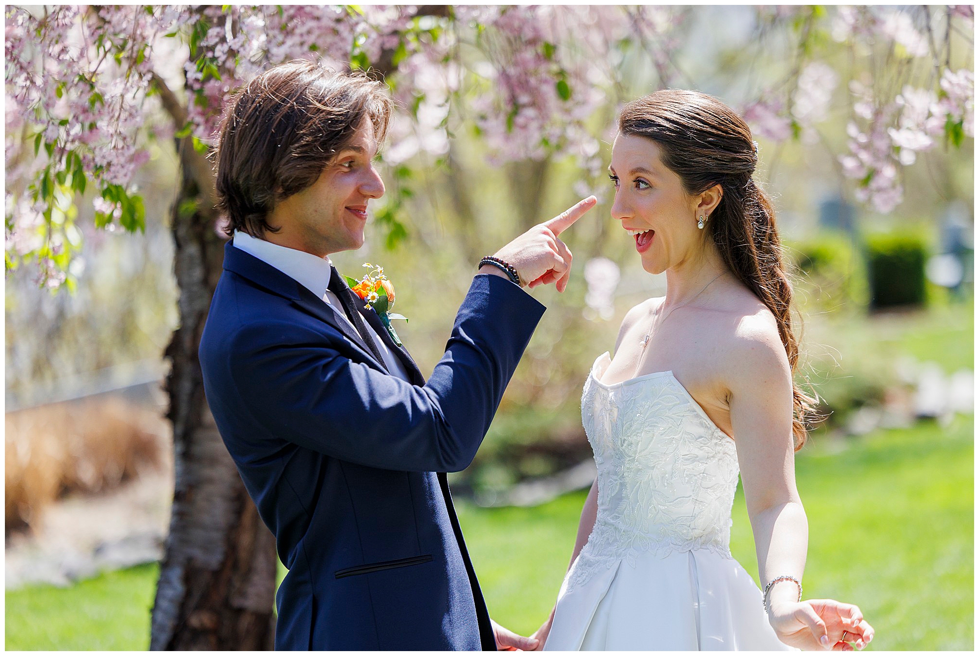 Bride and groom laughing face to face beneath a canopy of pink cherry blossoms at their April West Point wedding