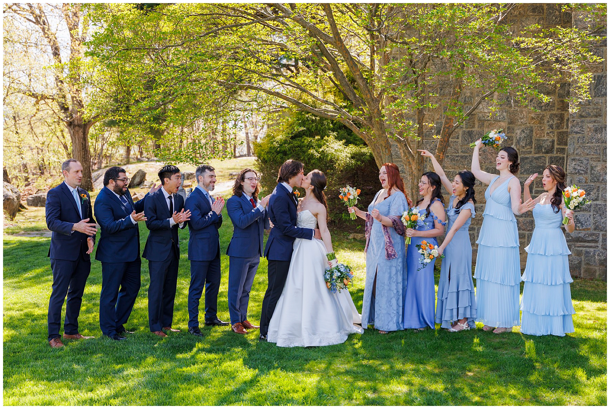 Bridesmaids in light blue dresses lined up for a group portrait on a spring green lawn at West Point