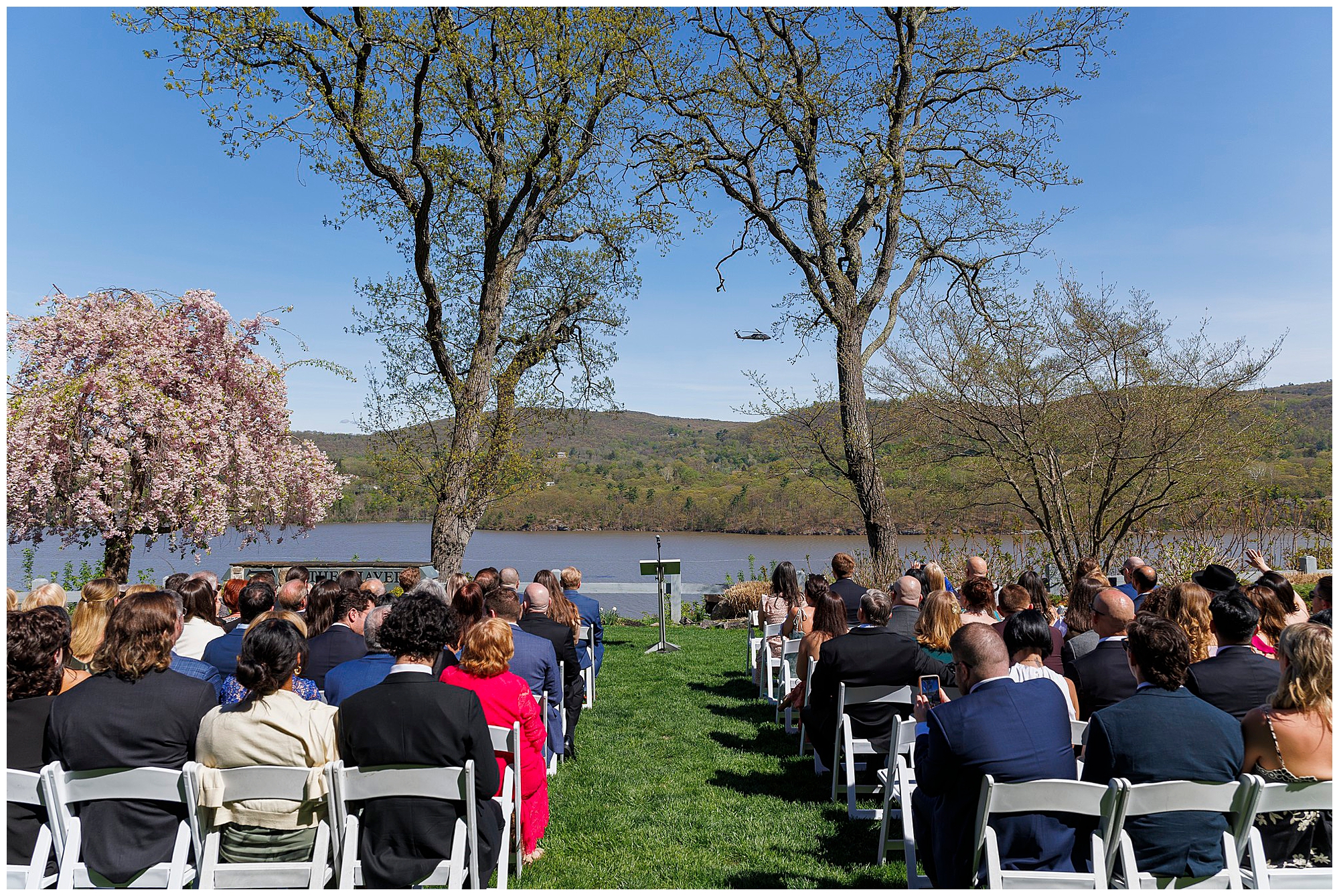 Wide shot of outdoor wedding ceremony at The Thayer Hotel at West Point with guests seated in white chairs on a sunny April day