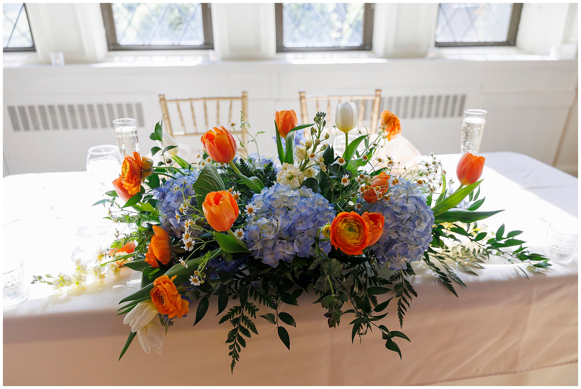 Elegant wedding centerpiece featuring blue hydrangeas, orange tulips, and white flowers arranged on a banquet table, captured by Hudson Valley wedding photographers specializing in wedding photography and videography