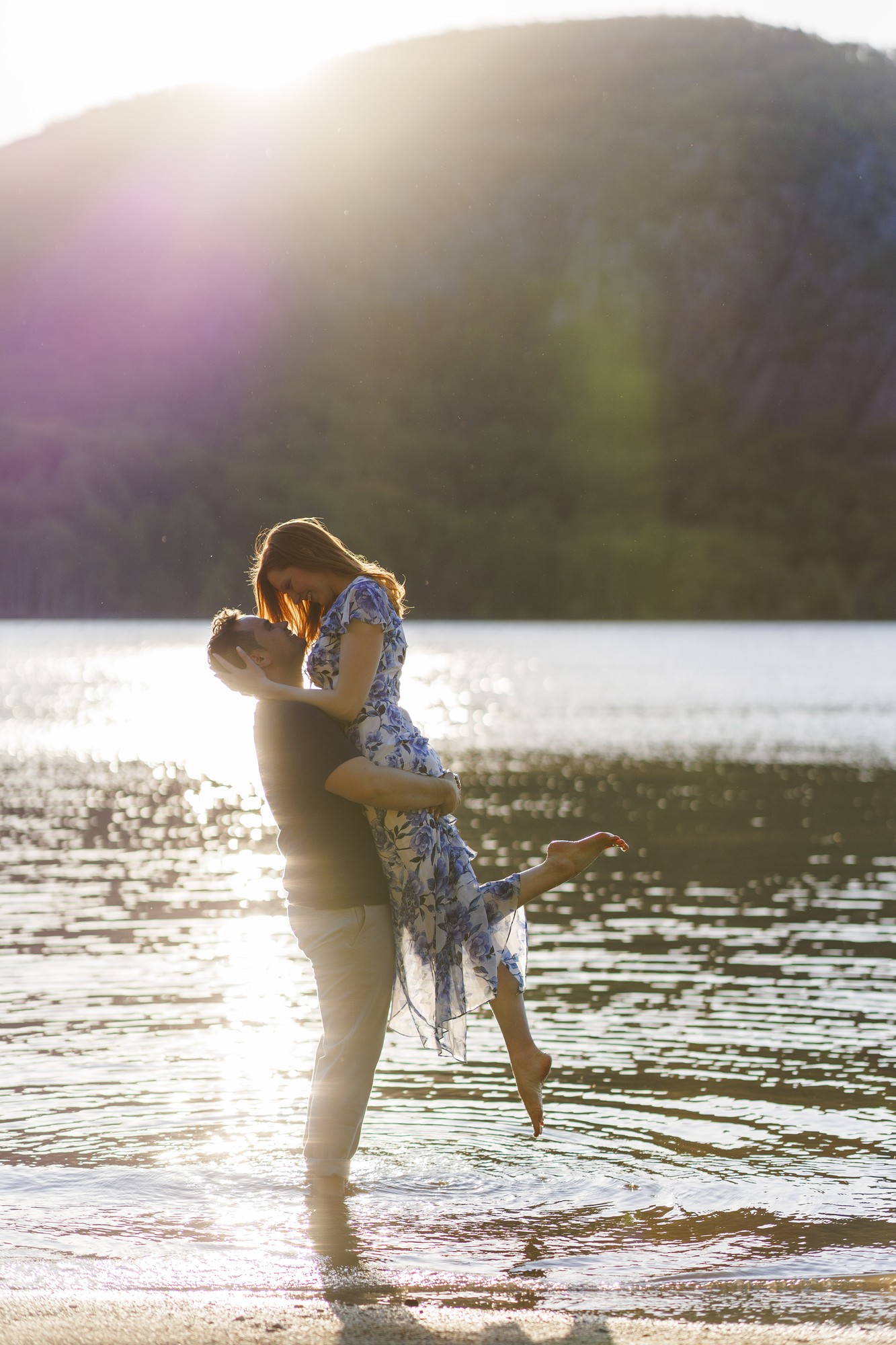 Couple embracing in lake water at sunset with forested mountain backdrop, Hudson Valley wedding photography style portrait