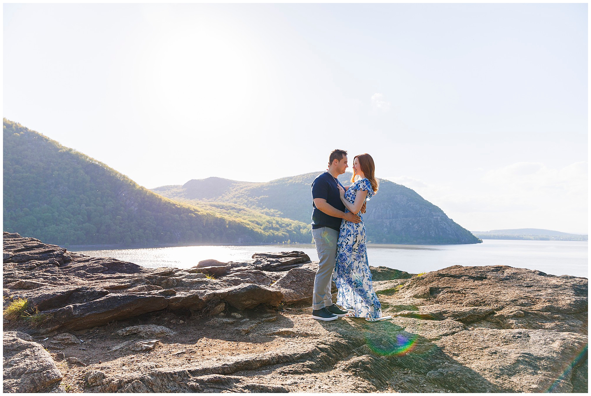 Couple embracing on rocky overlook with mountain lake backdrop during Hudson Valley wedding photography session