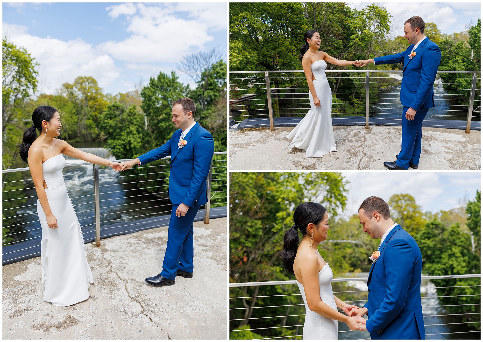 A bride in a white dress and a groom in a blue suit share a joyful first look outdoors, holding hands and smiling on a balcony at their roundhouse wedding, with green trees and water in the background.