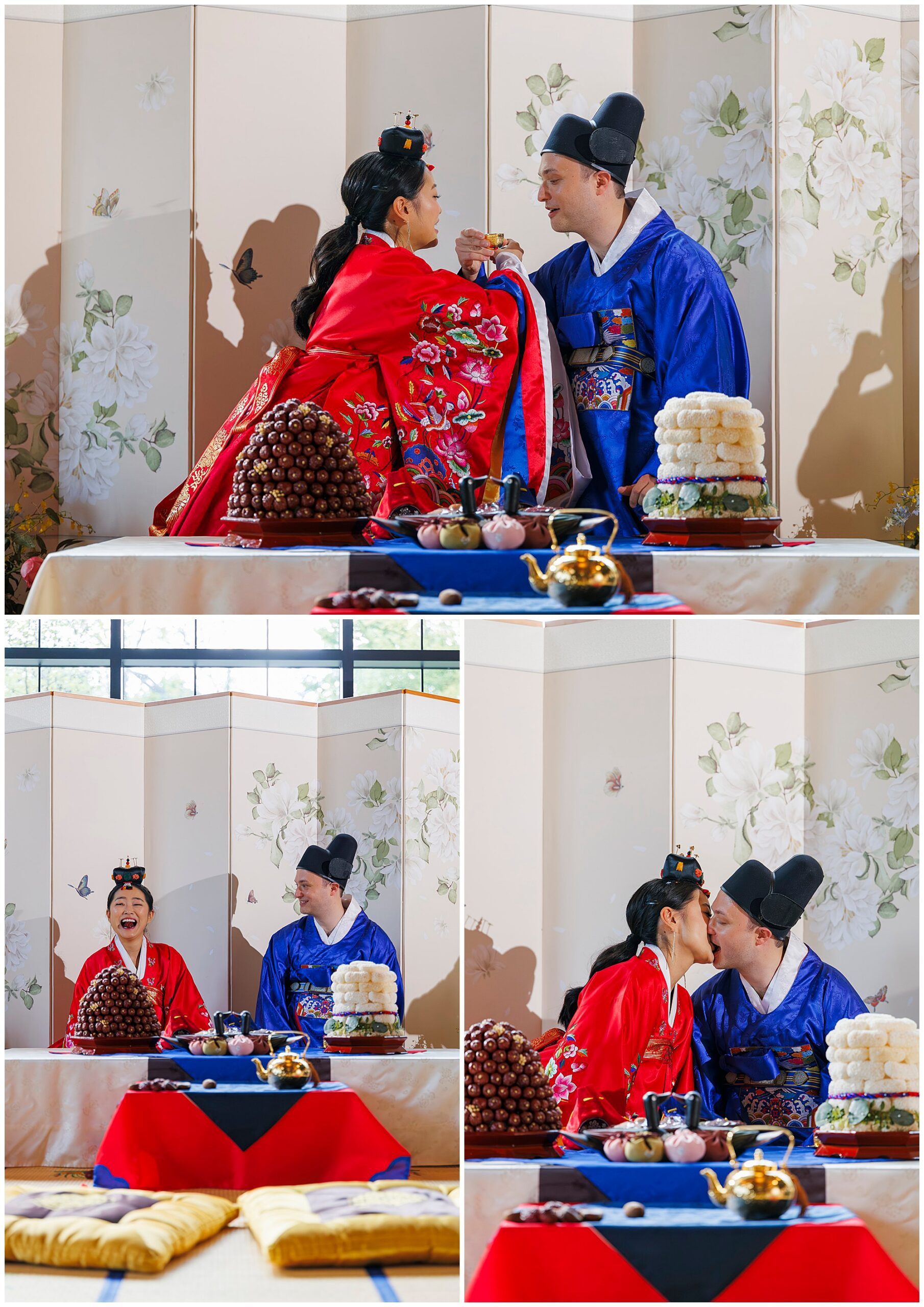 A bride and groom in traditional Korean wedding attire share a joyful moment, feeding each other and laughing at a decorated roundhouse wedding table with rice cakes and sweets, set against a floral screen backdrop.