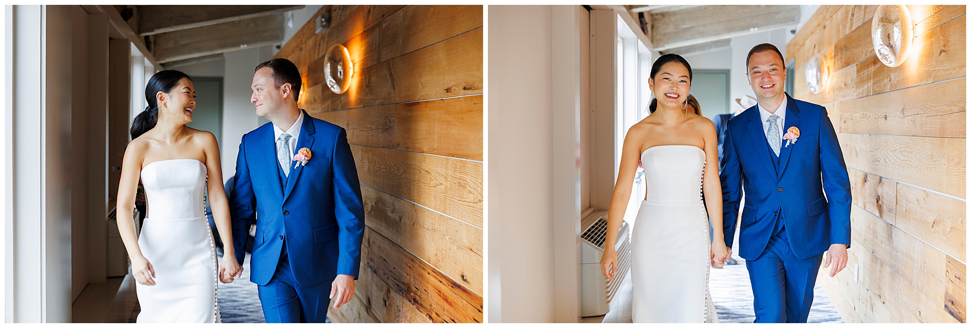 A couple dressed in wedding attire—a bride in a strapless white gown and a groom in a blue suit—walk hand in hand, smiling at each other, as they stroll through a modern, warmly-lit hallway at their roundhouse wedding.