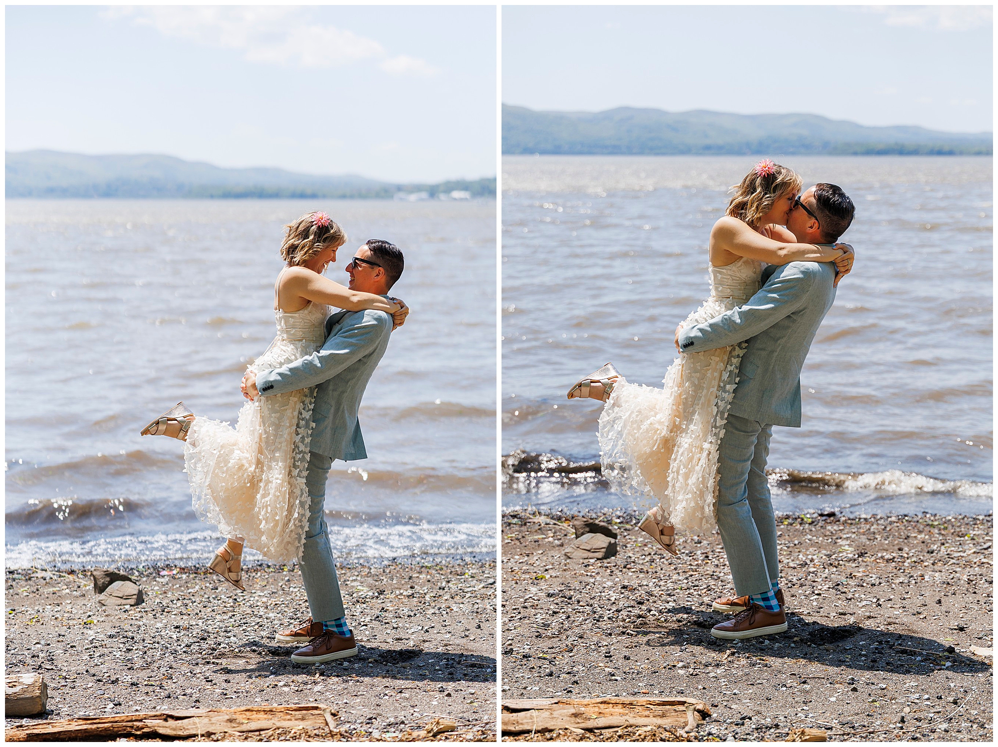 A groom in a light blue suit lifts and embraces his bride, who wears a white dress, on a pebbled lakeshore after their Beacon Courthouse elopement. Both look joyful and affectionate with mountains and a bright sky in the background.