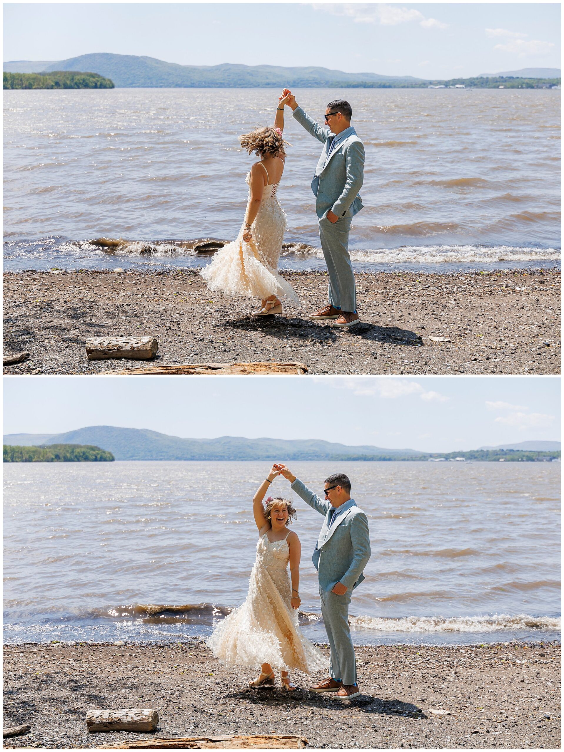 A couple dressed in wedding attire dances joyfully on a pebbled lakeshore, celebrating their Beacon courthouse elopement as the groom twirls the bride. The lake and distant hills are visible under a sunny sky.