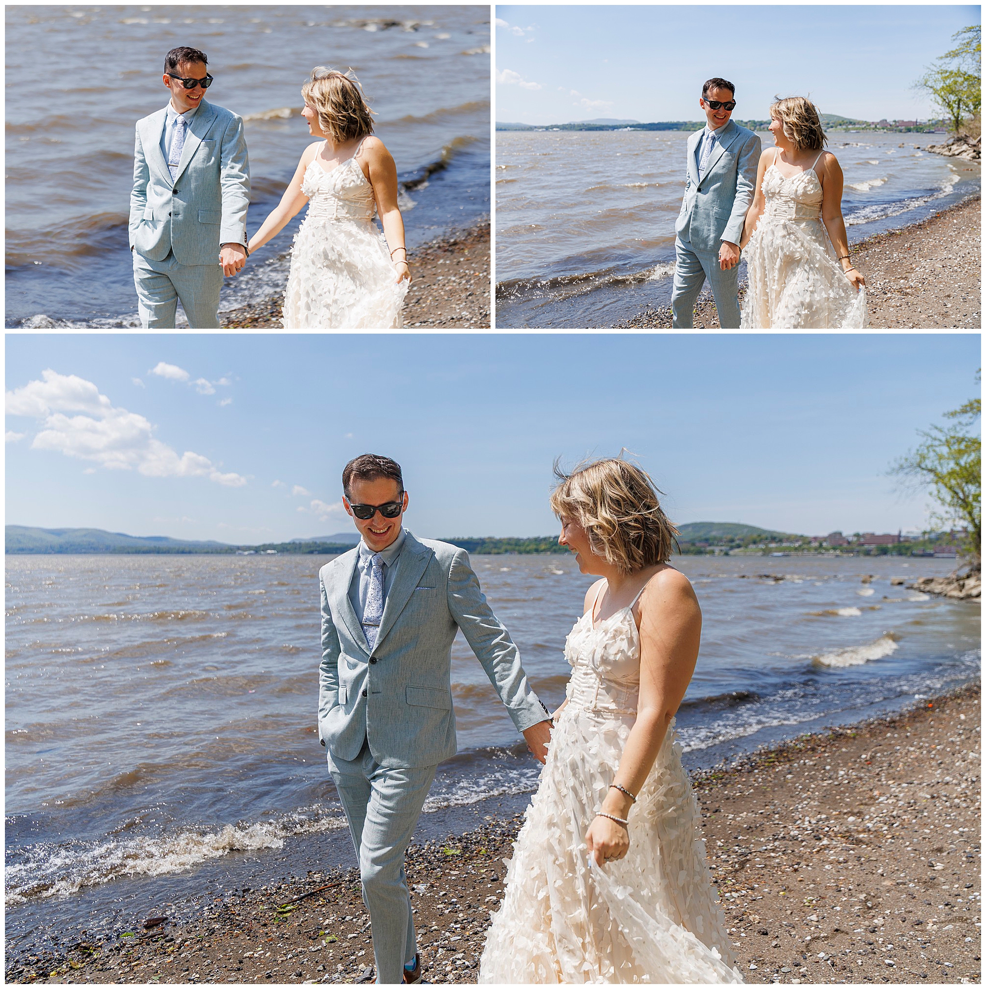A couple in wedding attire walks hand in hand along a sunny, pebbled lakeshore after their Beacon Courthouse elopement, smiling at each other with blue sky and gentle waves in the background.