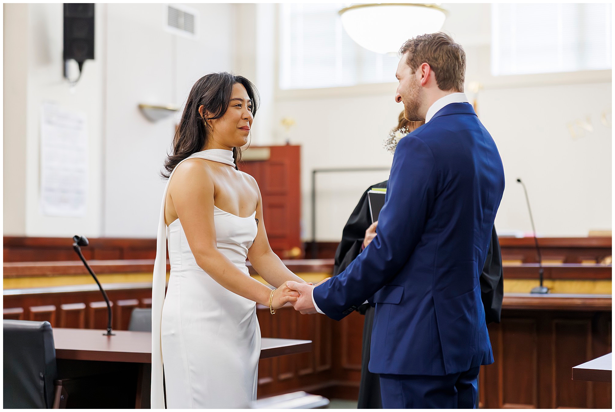 A bride and groom stand facing each other, holding hands in Beacon City Hall. Both dressed formally, they appear to be exchanging vows during their intimate elopement ceremony.