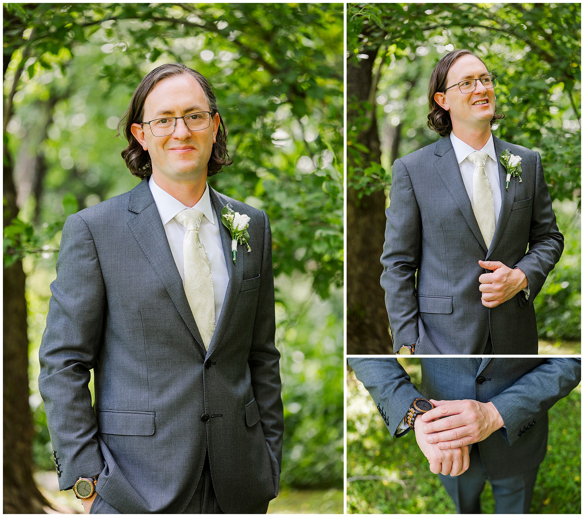 A man with glasses and shoulder-length hair, dressed in a gray suit with a white tie and boutonniere, stands outdoors among green trees at an Airbnb micro wedding, posing with hands in pockets, adjusting his jacket, and showing his wristwatch.