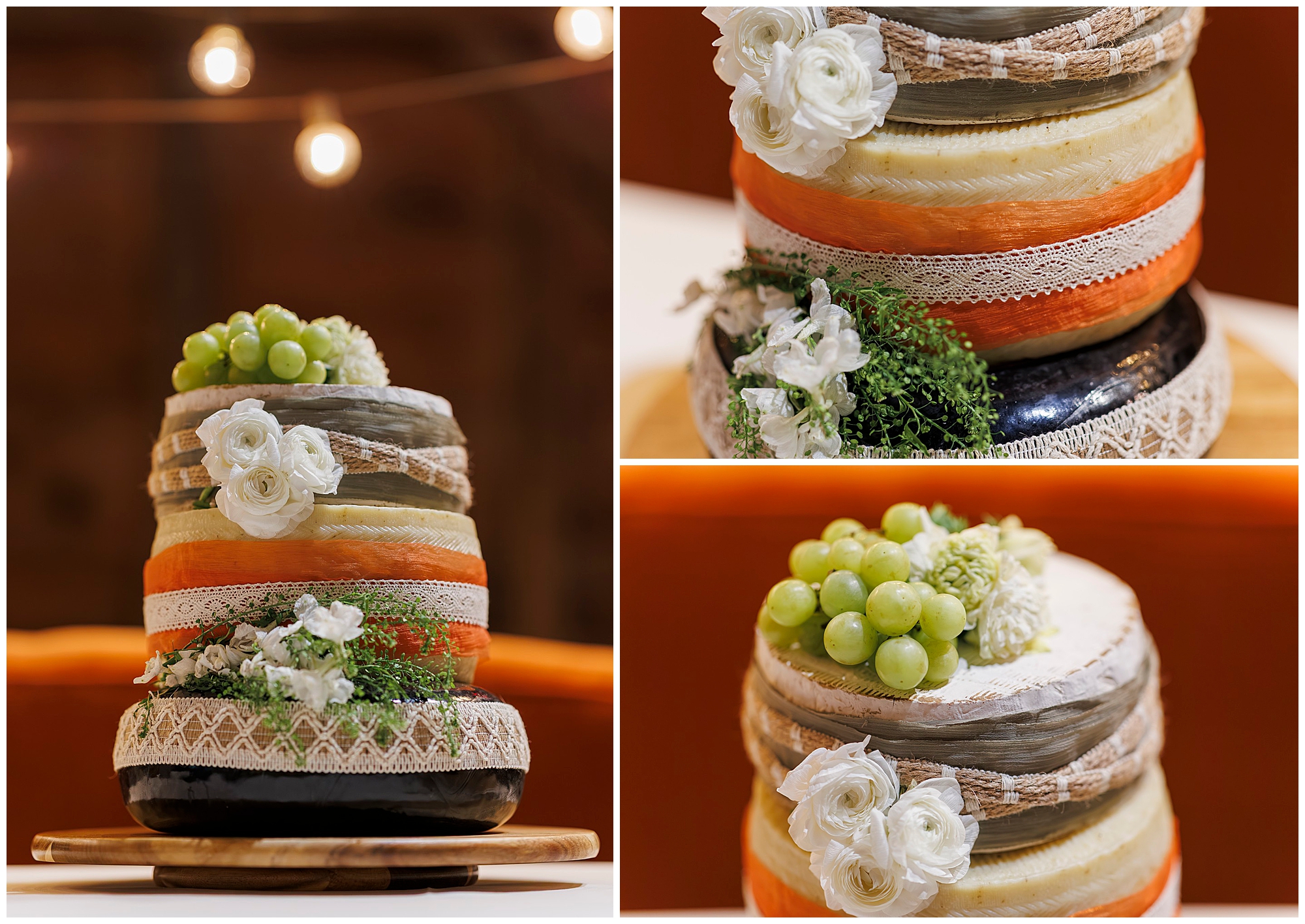 A three-tiered cheese wheel cake decorated with lace, white flowers, greenery, and a cluster of green grapes, displayed on a wooden board with warm string lights in the background.