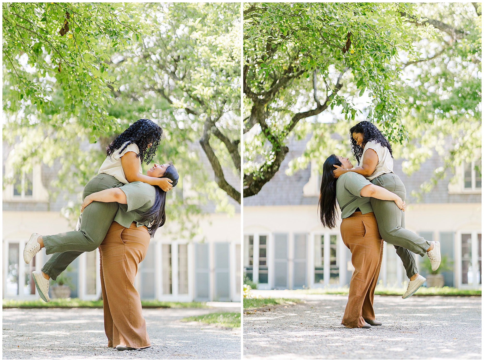 Two women smile joyfully as one lifts the other off the ground under a green leafy tree, with a sunlit building and blue shutters behind them—capturing LGBTQ engagement photos at Stonecrop Gardens.