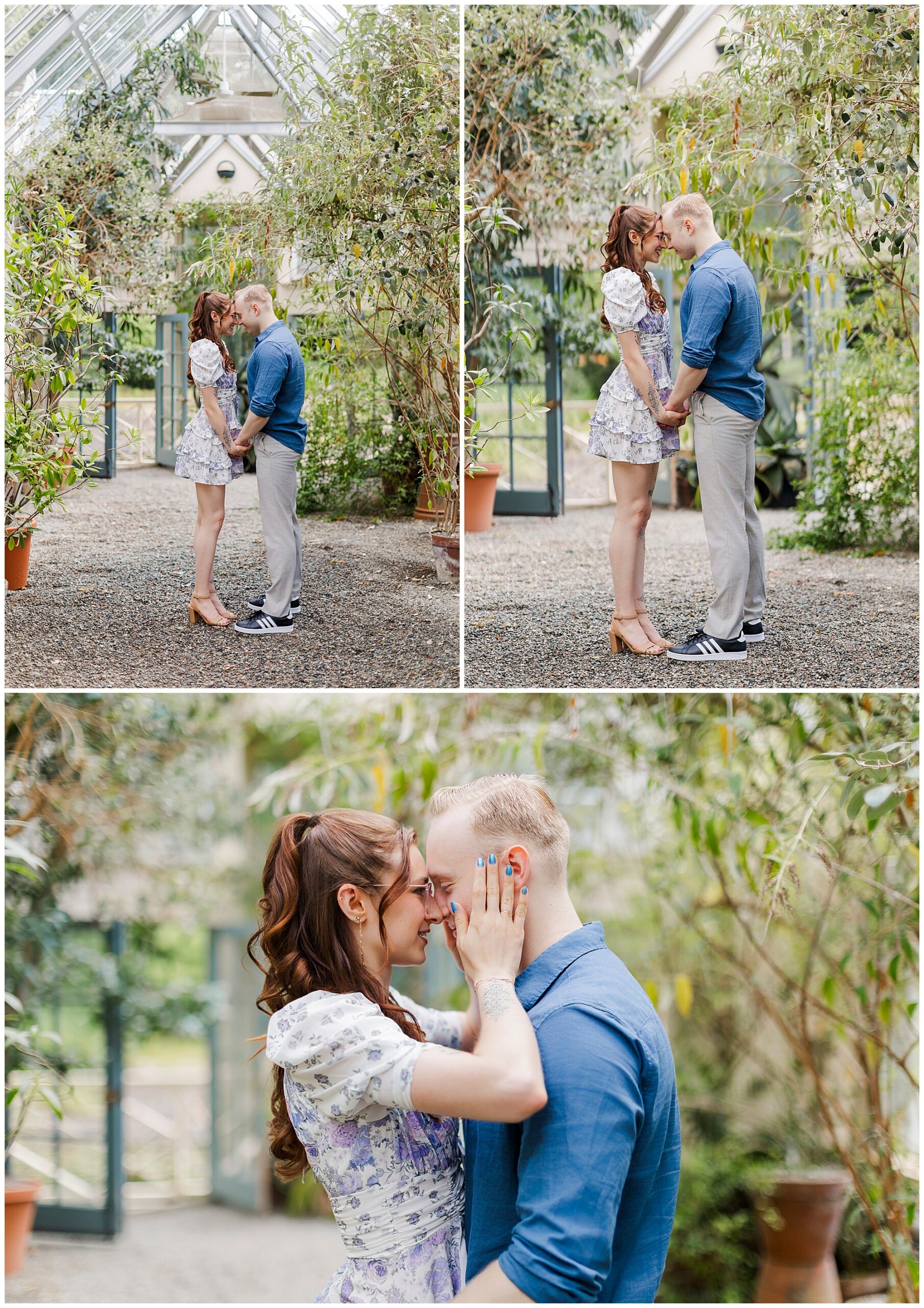 A couple stands close together in a greenhouse at Stonecrop Gardens, holding hands and touching foreheads, smiling affectionately. The woman wears a floral dress and heels; the man wears a blue shirt and light pants. Lush green plants surround them.