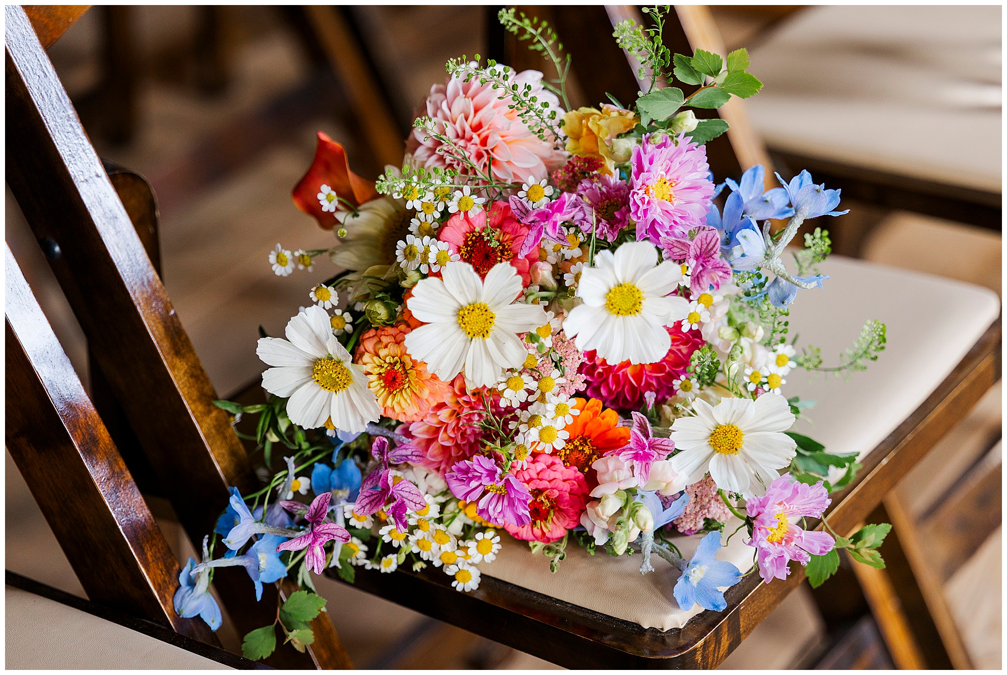 A colorful bouquet of wildflowers, including daisies and zinnias, rests on a wooden chair with a cushioned seat—perfect for capturing the rustic charm of a Knotting Hill Farm wedding.