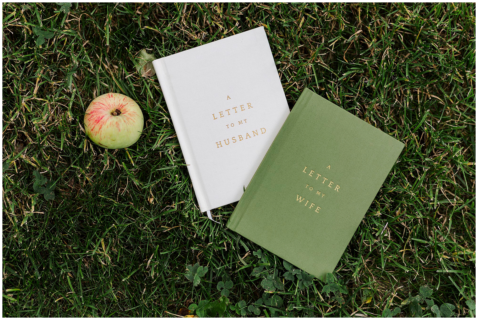 Two books titled A Letter to My Husband and A Letter to My Wife lie on grass next to an apple, evoking the heartfelt moments of a Knotting Hill Farm wedding.