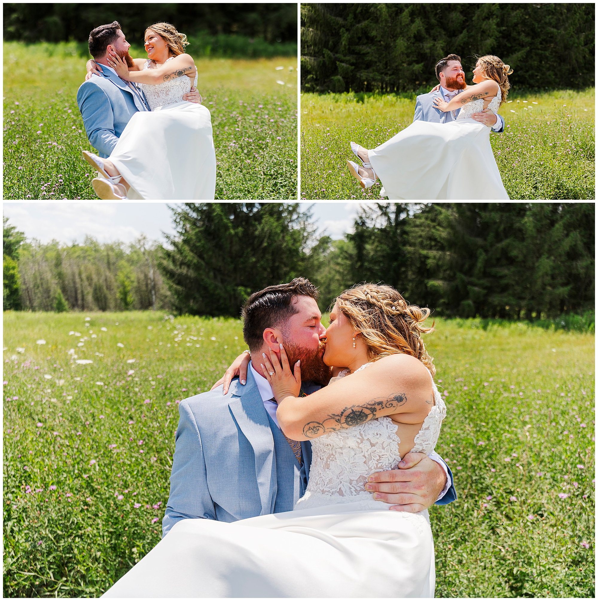 A groom in a light blue suit holds his bride in a white dress as they laugh and kiss, sitting together in a sunny, grassy field with wildflowers and trees in the background at their Knotting Hill Farm wedding.