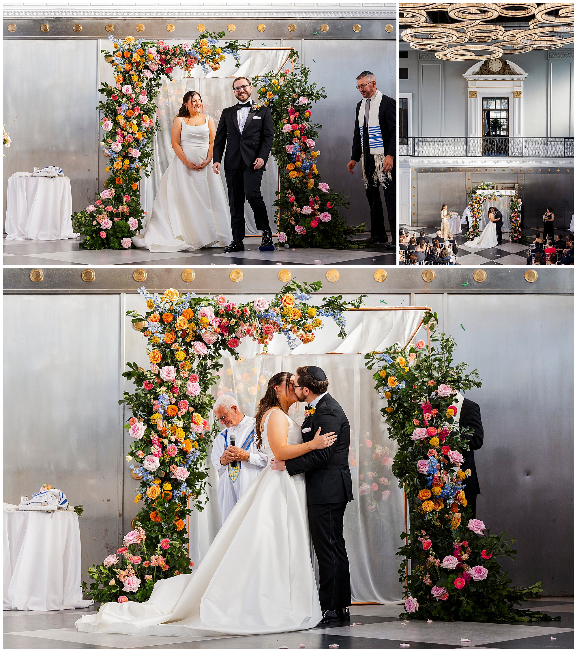 A bride and groom stand under a colorful floral arch during their felina wedding ceremony, exchanging vows and kissing, with guests seated and an officiant present. The venue has elegant silver walls and ornate ceiling decor.