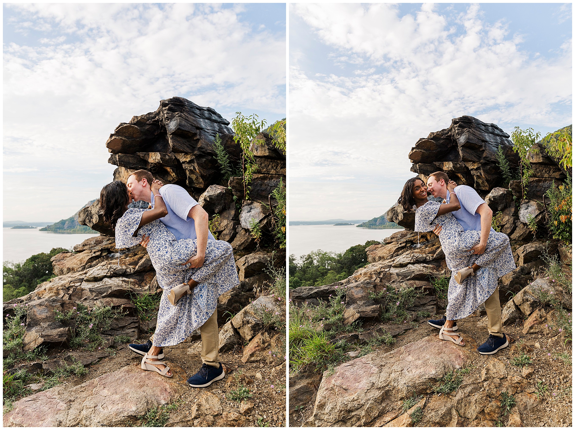 A couple stands on rocky terrain by a lake during their Cold Spring Engagement Shoot, with the man dipping and kissing the woman. They both smile, surrounded by greenery and a partly cloudy sky.