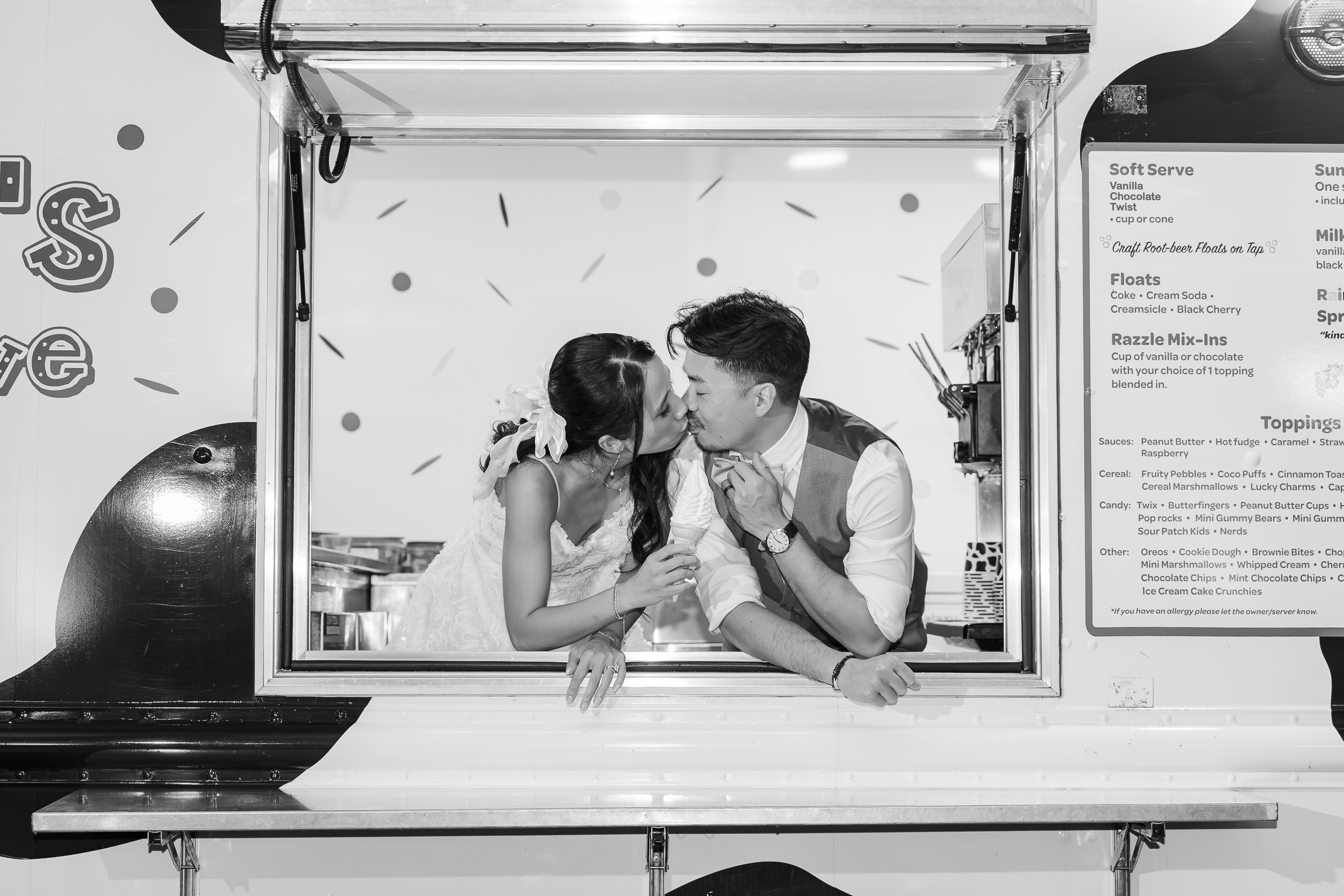 A bride and groom share a kiss while leaning out of an ice cream truck window, holding ice cream cones and smiling in a joyful, playful moment.