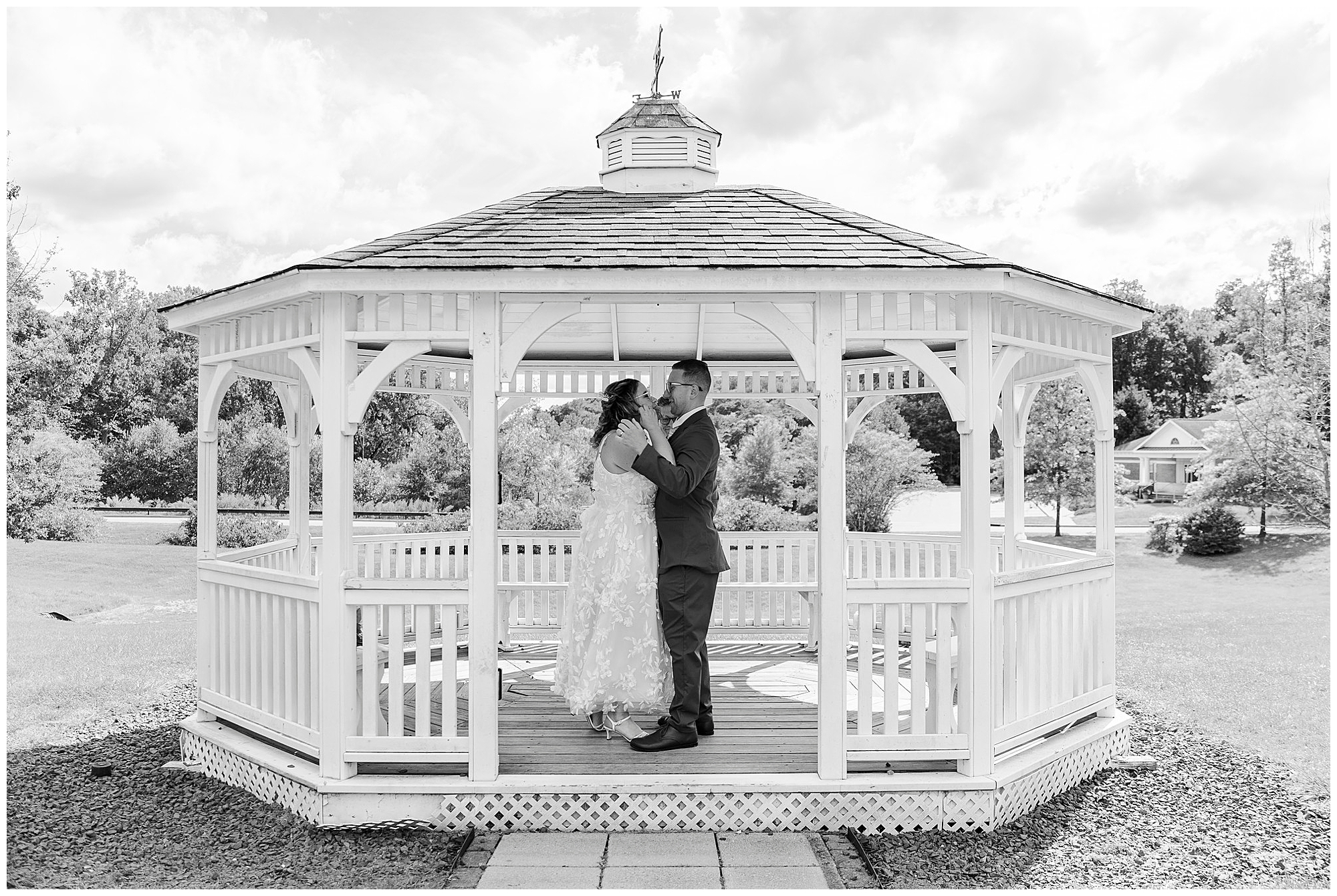 Bride and groom embrace inside the white gazebo, looking at each other on a sunny day.