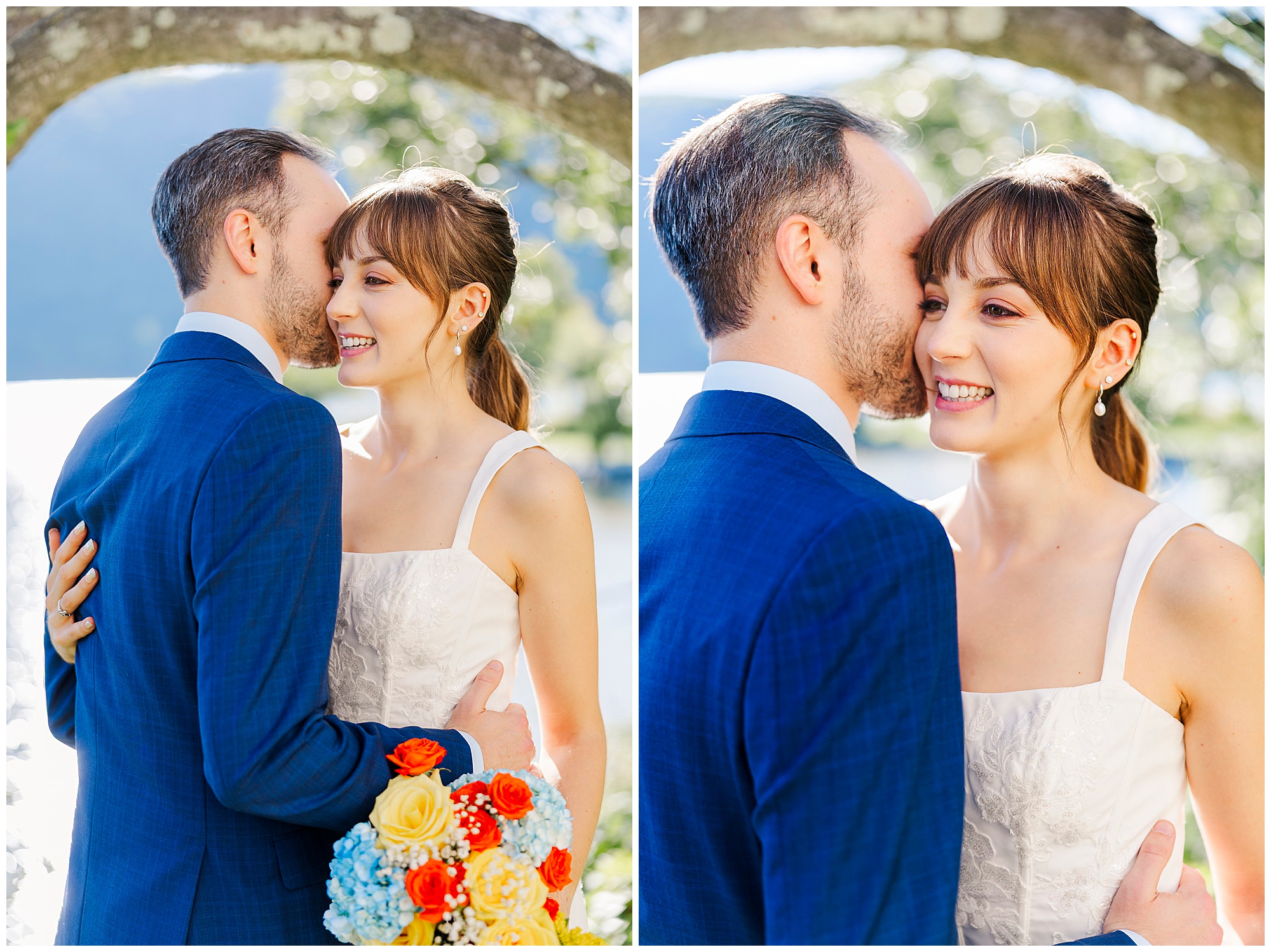 Groom in a blue suit whispers to his smiling bride as she holds a bouquet of yellow, orange and blue flowers.