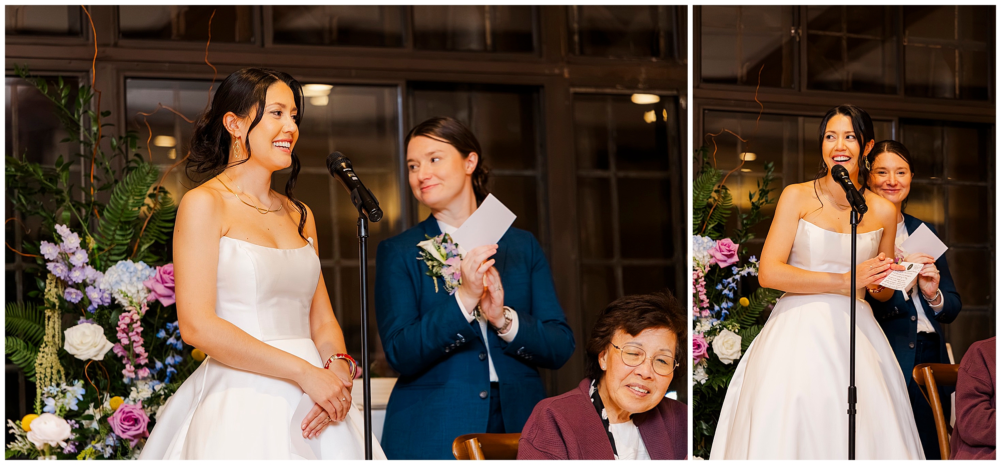 A bride in a white dress speaks at a microphone, smiling, while her partner in a blue suit stands nearby clapping. A seated older woman is in front. Flowers decorate the background.