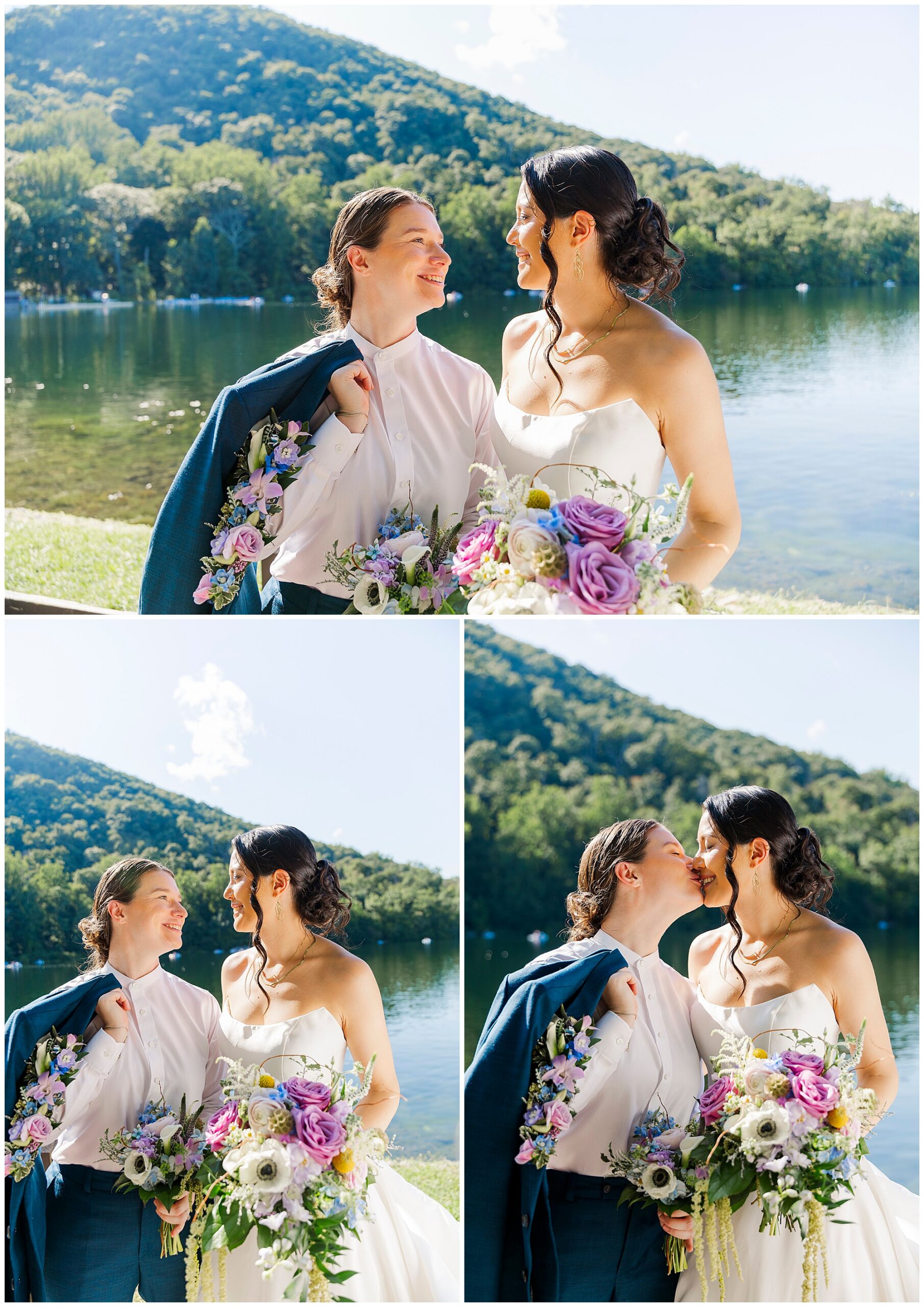 Two brides smile with their bouquets by the lake, one draping her blue jacket over the other's shoulders, green hills behind them.