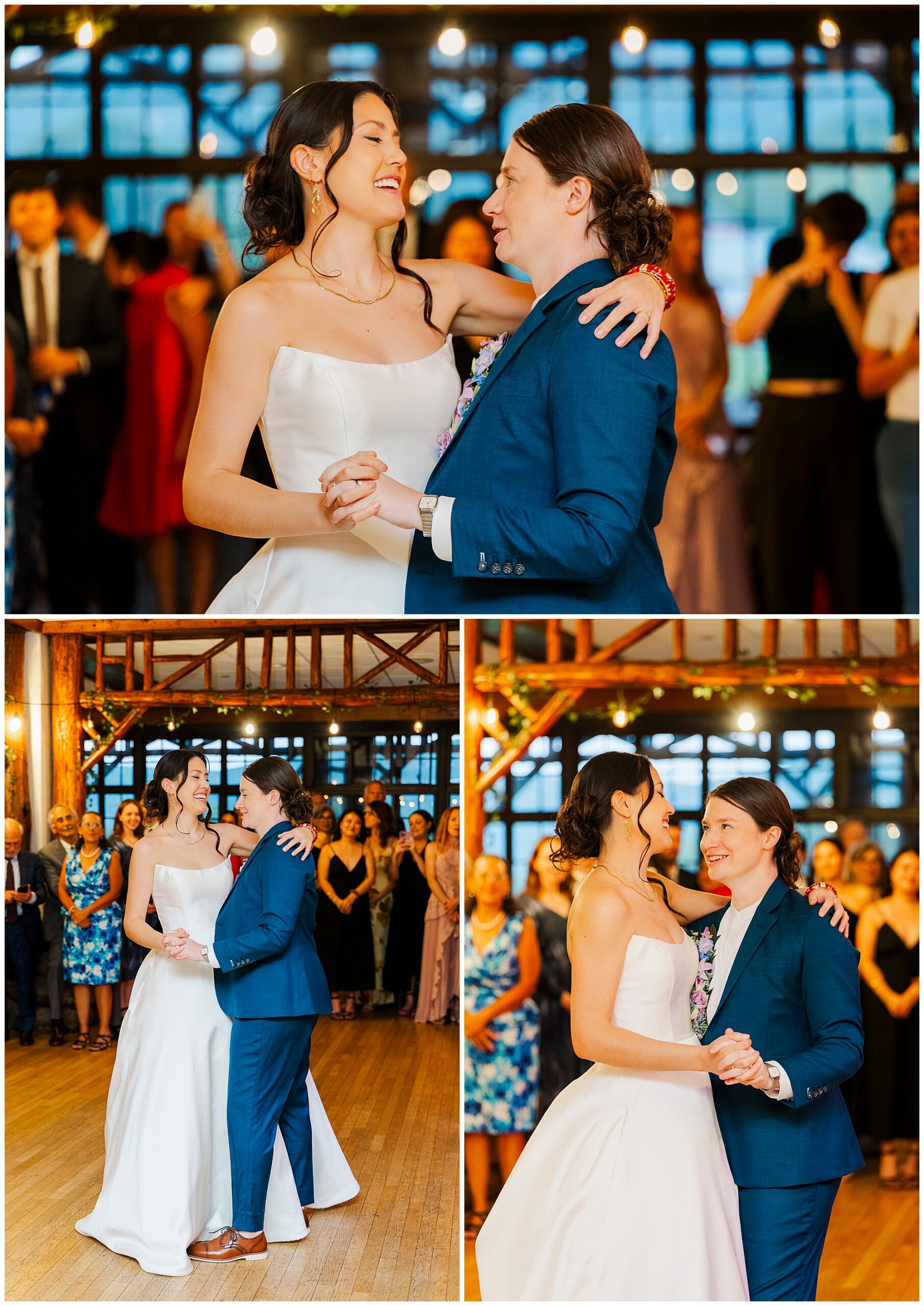 Bride in a white dress and bride in a blue suit share their first dance in the rustic hall at Bear Mountain Inn, surrounded by smiling guests.