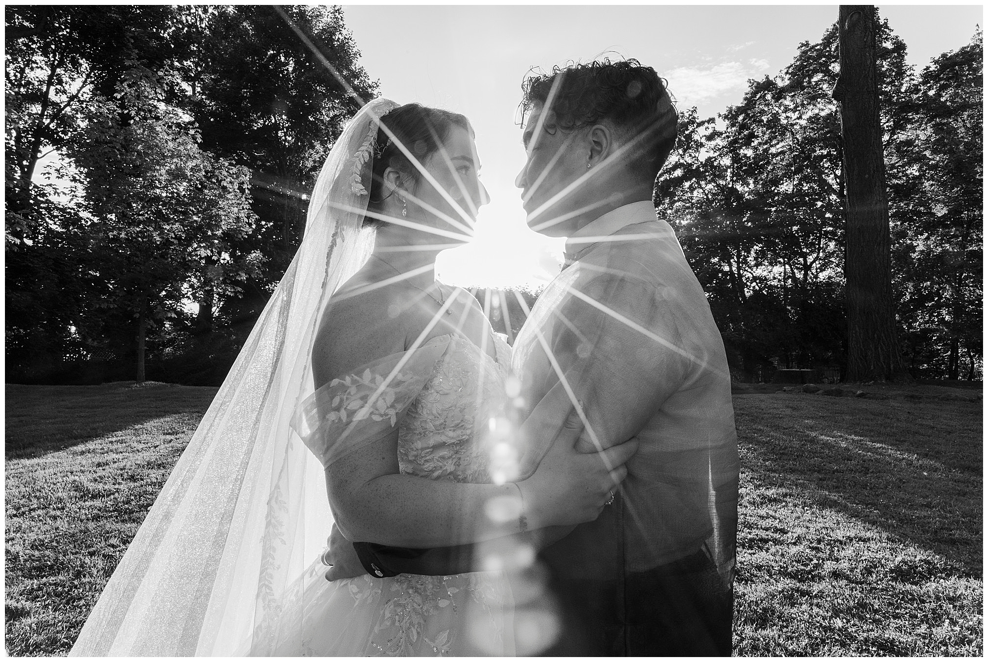 Bride and groom embrace at sunset with the sun bursting into a starburst between them and trees behind.