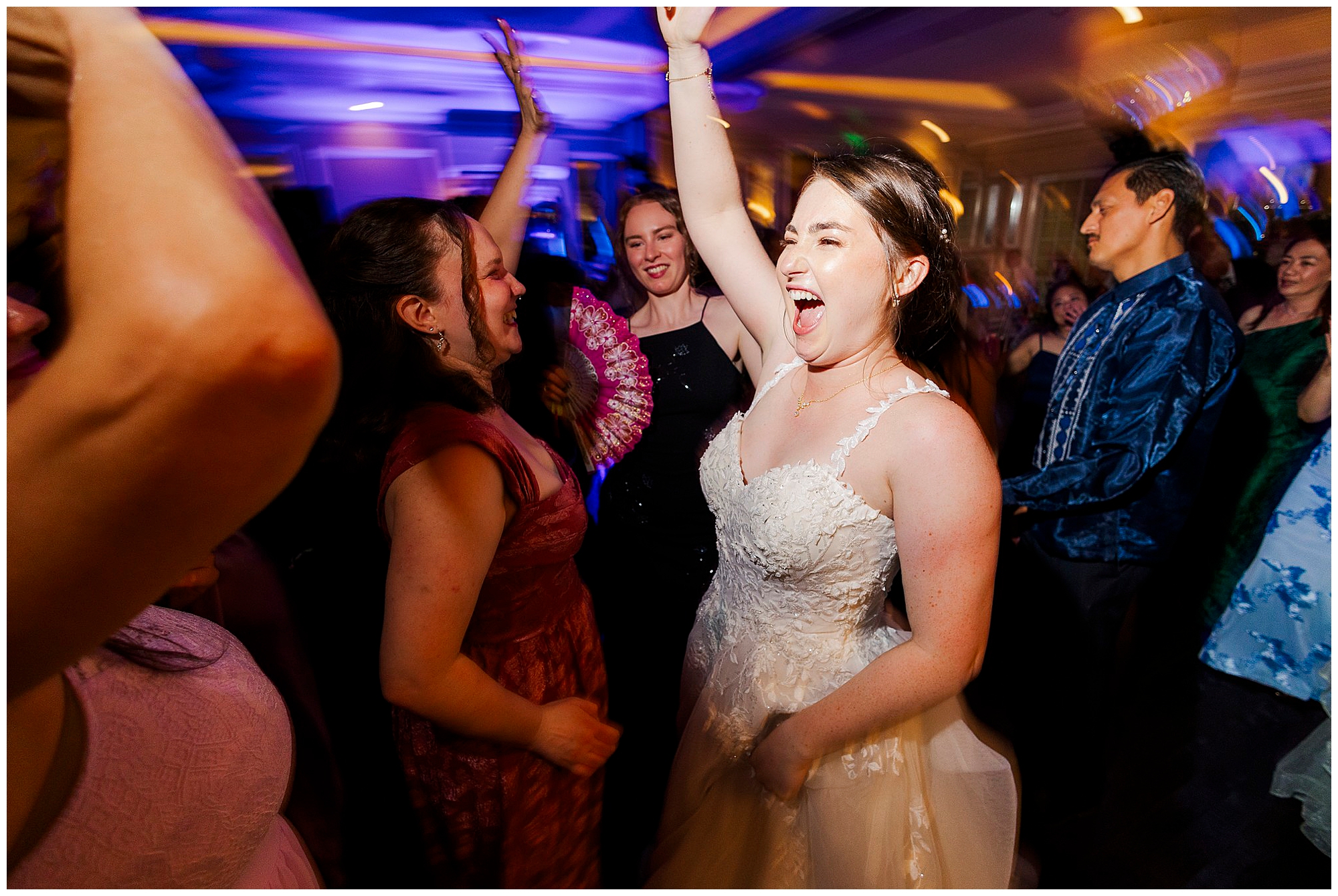 Joyful bride dances with friends in colorful outfits under vibrant lights.