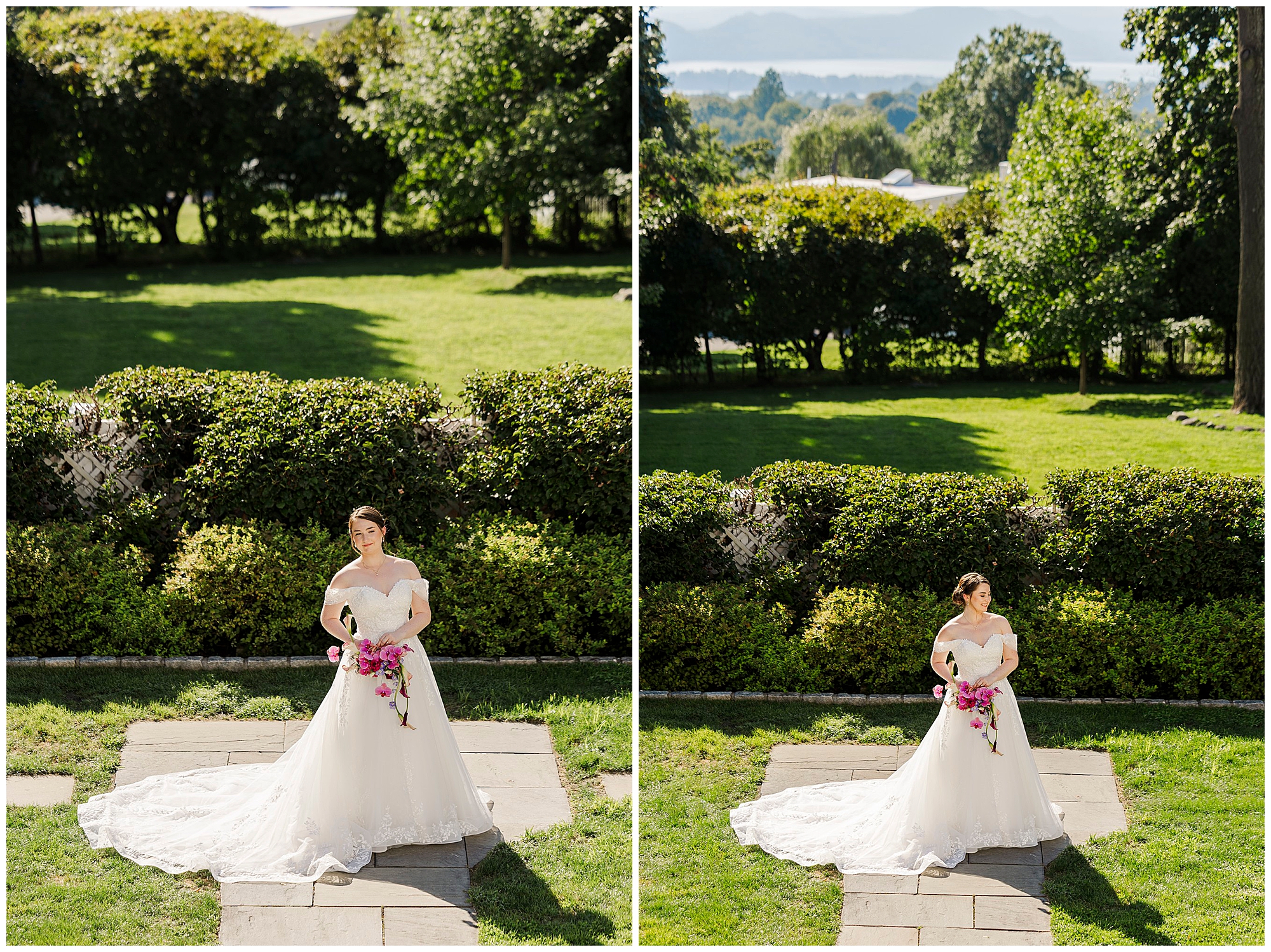 Bride in a white gown stands on a stone path holding a bouquet of pink flowers, with green grass and hedges behind her.