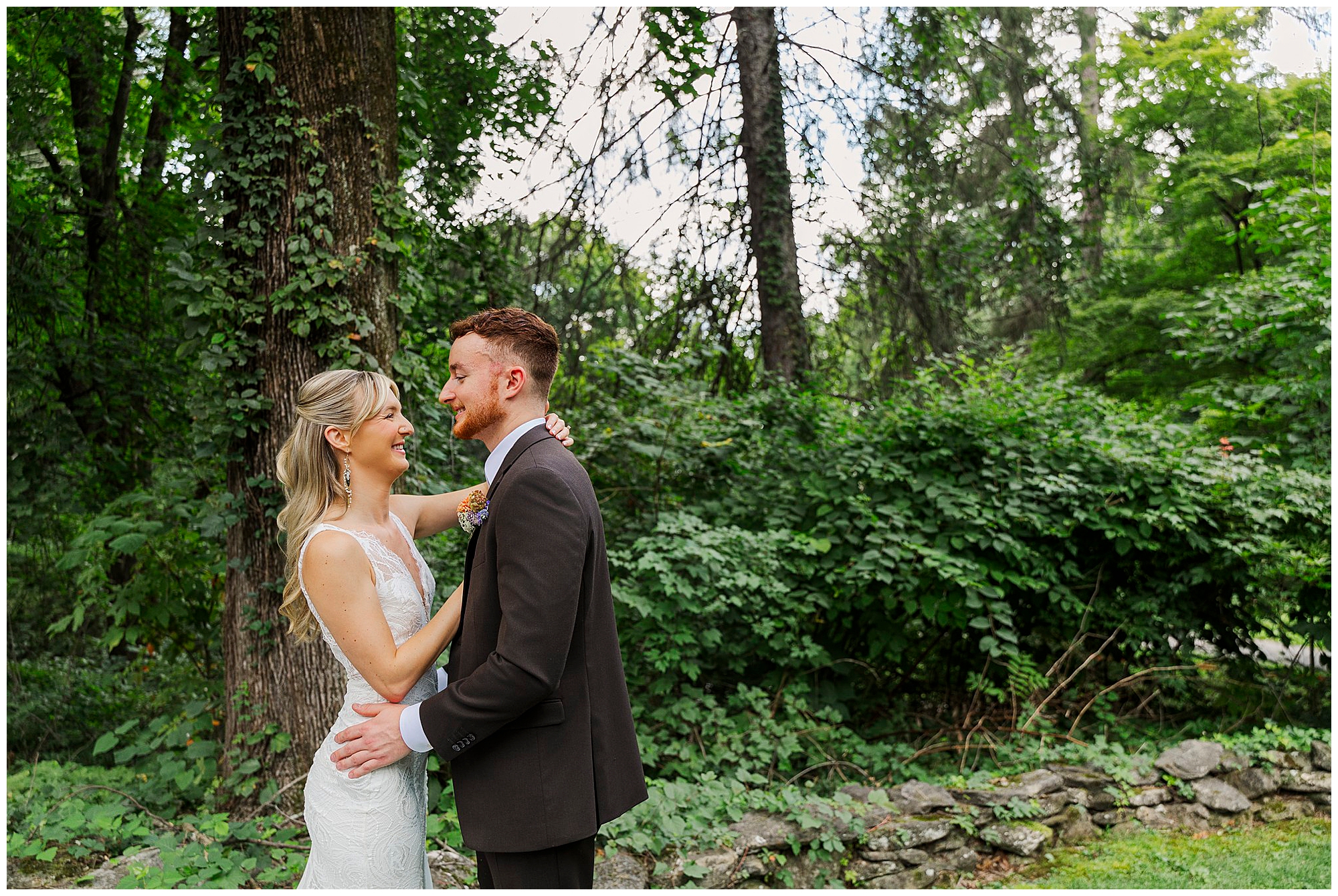 Bride and groom smile at each other while embracing, with trees and vines behind them.