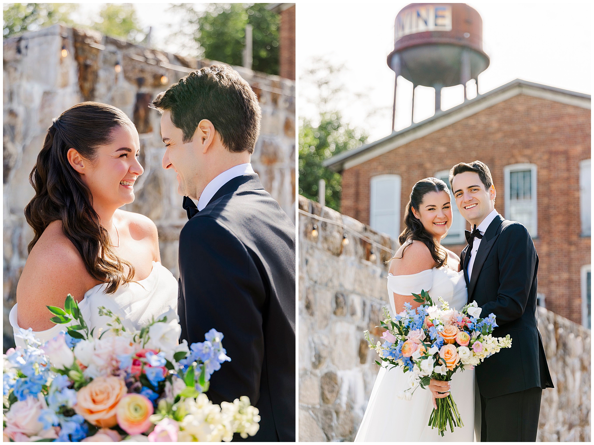A bride and groom stand outdoors, smiling at each other and posing with a colorful bouquet. A stone wall and brick building with a large water tower are visible in the background.