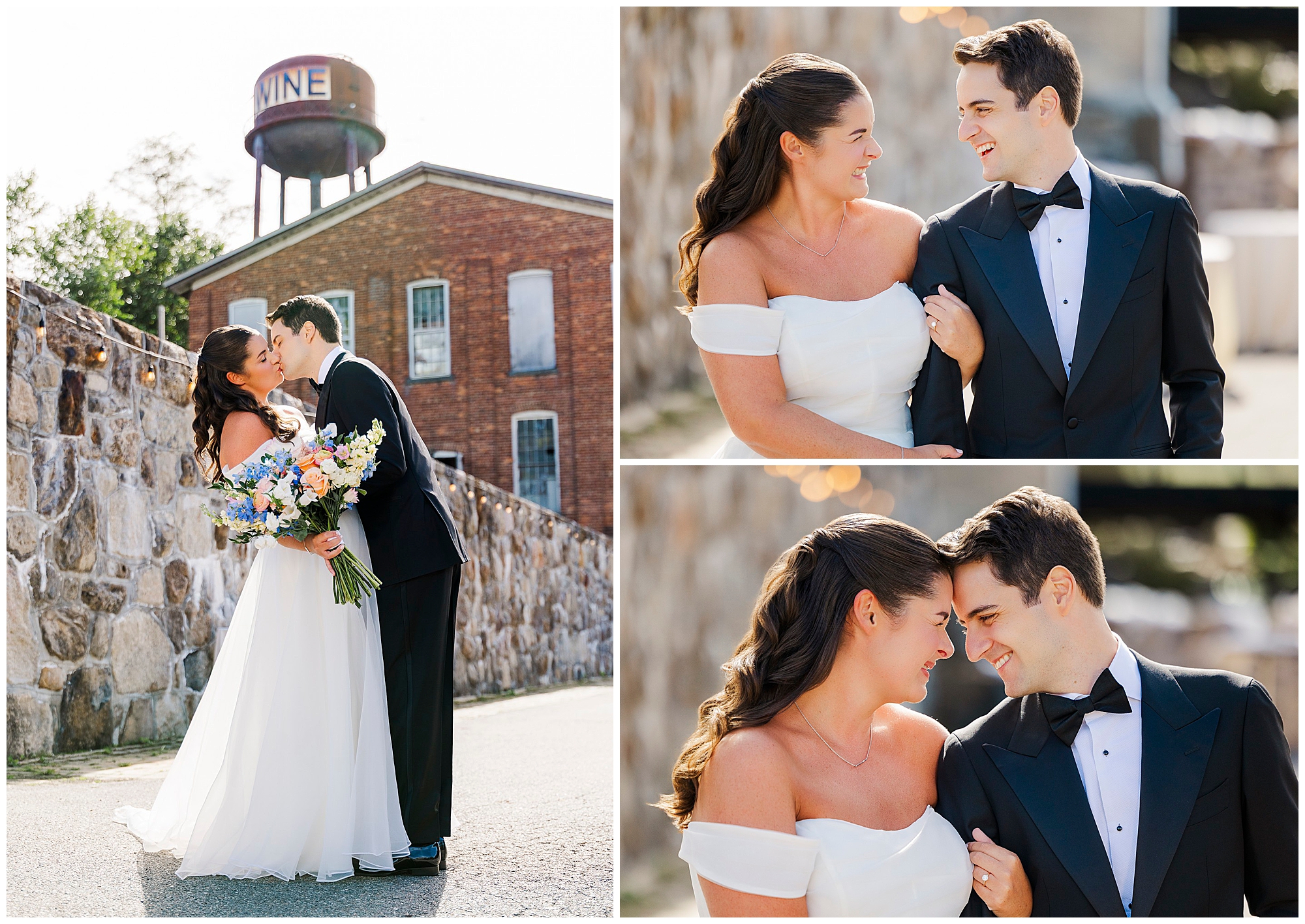 A bride and groom smile and embrace outdoors, dressed in wedding attire. They stand by a stone wall, with a brick building and water tower in the background.
