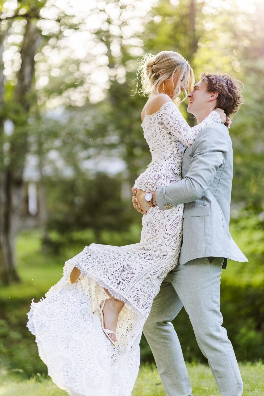 Groom lifting his bride in her lace gown during couple portraits in soft evening light